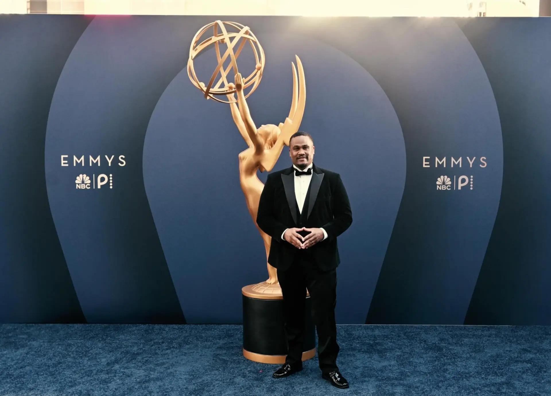 E'Ian West in a tuxedo beside the Emmy statue on the Emmys red carpet at the NBC and Peacock step and repeat E'Ian West in a tuxedo beside the Emmy statue on the Emmys red carpet at the NBC and Peacock step and repeat
